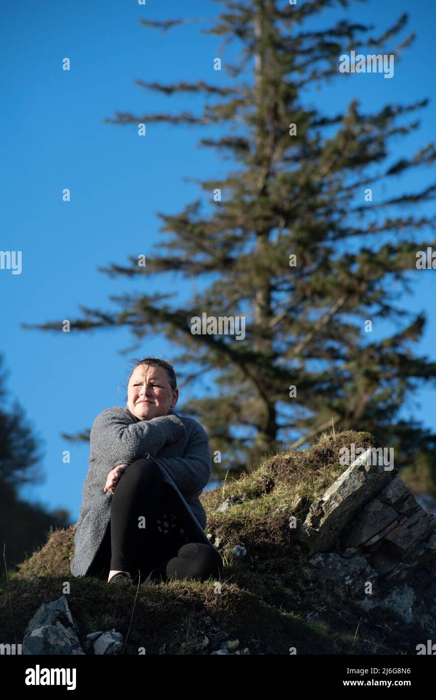 Frau, die sich auf moosigen Felsen unter der schottischen Kiefer vor blauem Himmel entspannt Stockfoto