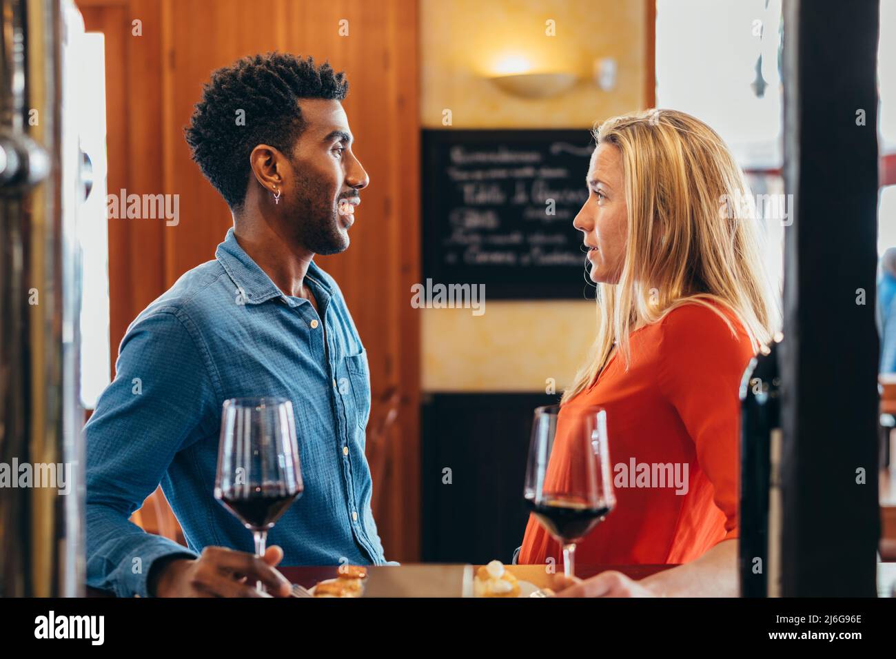 Ein multiethnisches Paar plaudert an der Restaurantbar, während es Rotwein trinkt Stockfoto