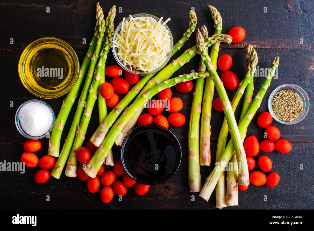 Caprese gerösteter Spargel Zutaten auf einem Tisch aus dunklem Holz: Frischer Spargel, Traubentomaten und andere Zutaten auf dunklem Grund Stockfoto
