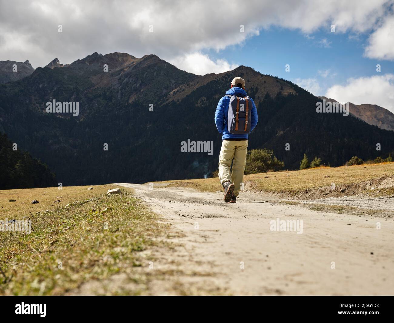 Rückansicht des asiatischen Wanderreisenden Rucksacktouristen, der auf einer unbefestigten Straße in Richtung Berge und Wald geht Stockfoto