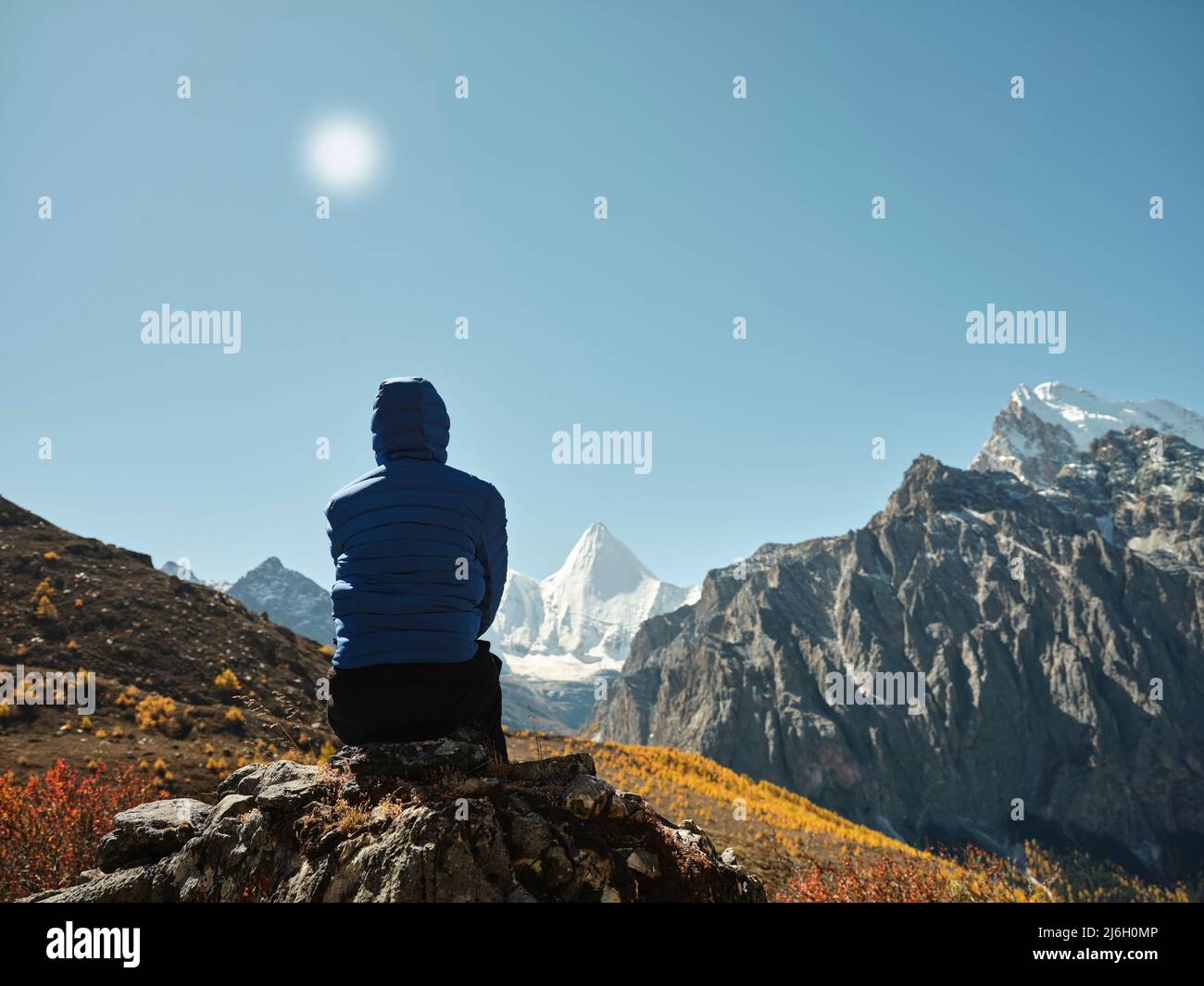 Rückansicht einer asiatischen Frau, die auf einem nahe gelegenen Berg sitzt und den Berg Yangmaiyong (oder Jampayang auf Tibetisch) in Yading, Kreis Daocheng, Sichua, anschaut Stockfoto