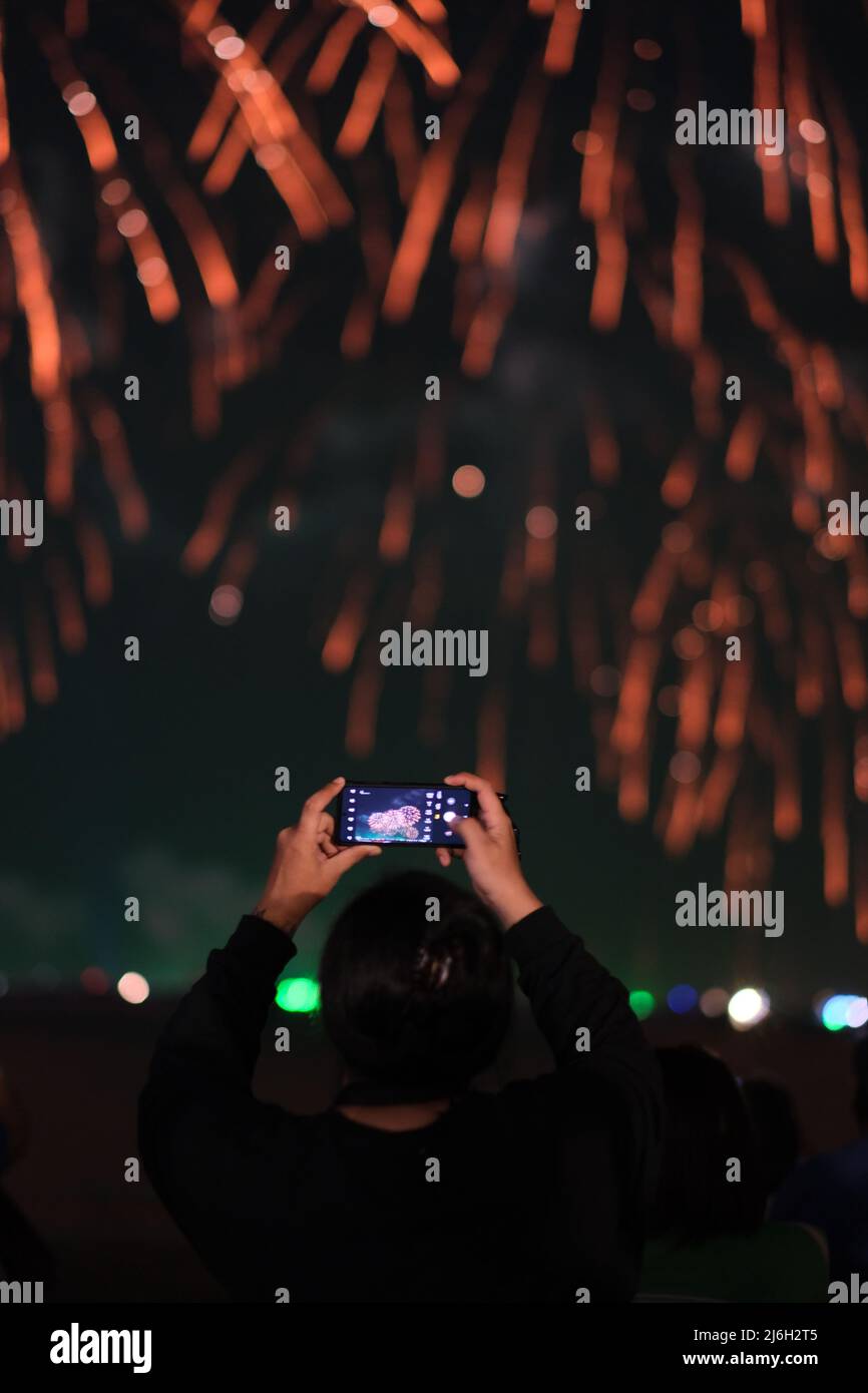 Eine zufällige Person aus der Menge zeichnet mit ihrem Smartphone ein Feuerwerk auf Stockfoto