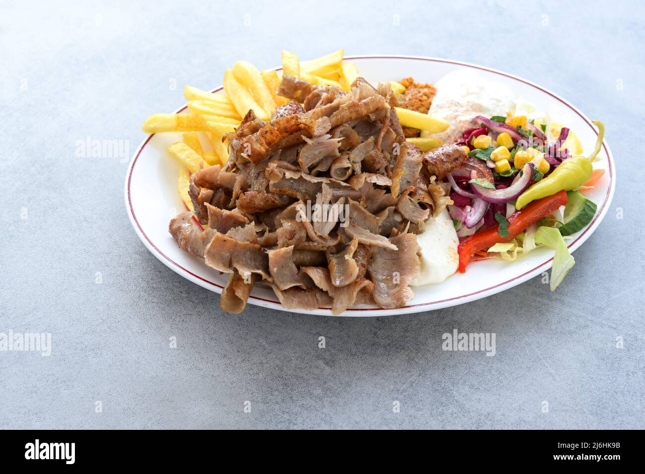 Dünne Scheiben Döner-Kebab-Fleisch mit pommes frites, Salat und Joghurt-Dip-Sauce auf einem Teller und einem grauen Tisch, Kopierraum, ausgewählter Fokus, enge Tiefe von Stockfoto
