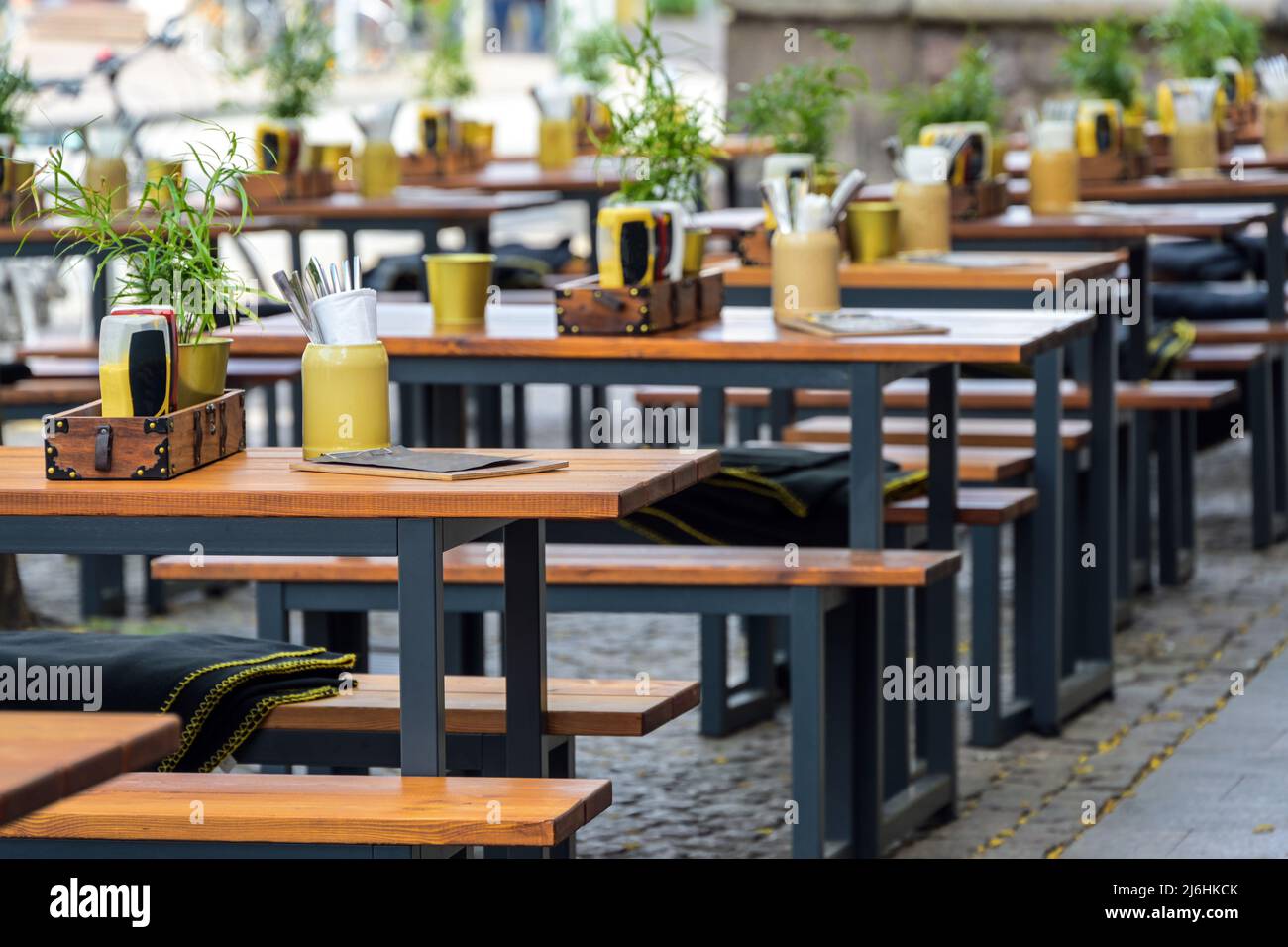 Holzbänke und gedeckte Tische in einem Straßenrestaurant im Stadtzentrum, städtische Outdoor-Gastronomie, ausgewählter Fokus, enge Schärfentiefe Stockfoto