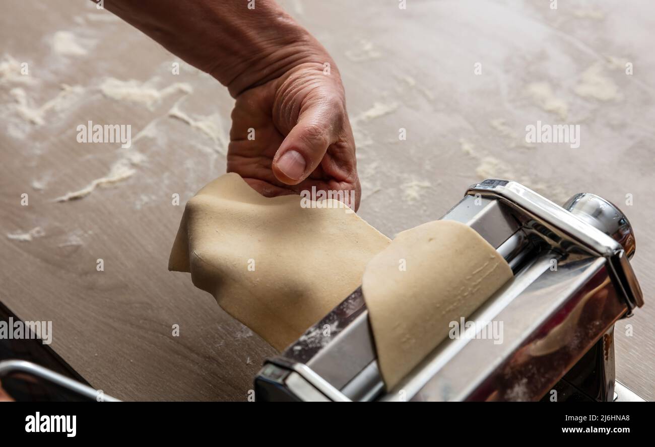 Pasta-Maschine. Frische Pasta hausgemachte Zubereitung. Männliche Hand macht Teig phylo Nahaufnahme Stockfoto