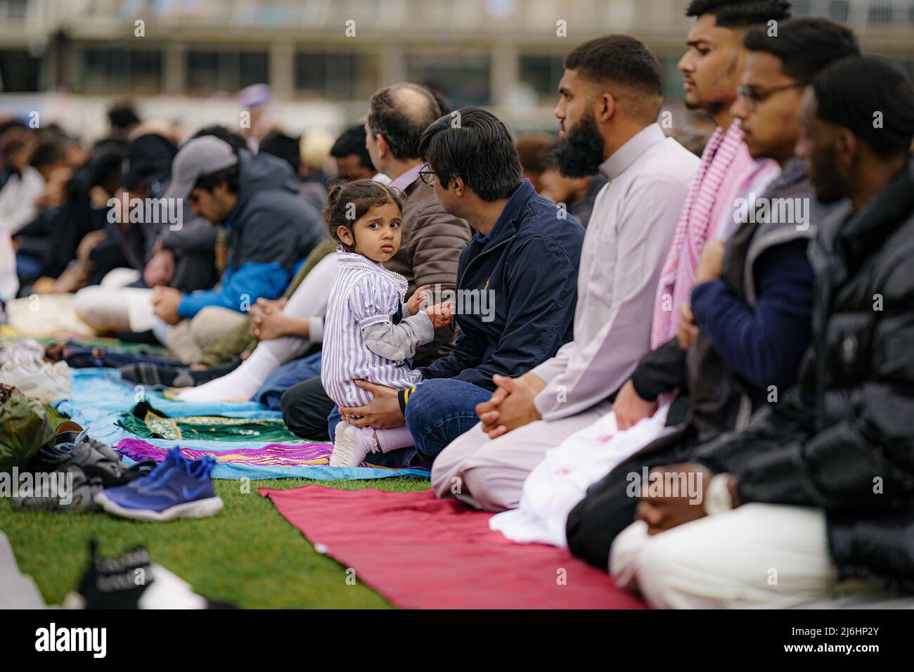 Die zweijährige Nuriya Faraz sitzt mit ihrem Vater, während sich Menschen während der Sunnah im Eid-Gebet versammeln, während sie im Freien im Big Eid Salah in Bristol beten: Eid al-Fitr 2022, als der heilige Monat Ramadan zu Ende geht und Muslime Eid al-Fitr feiern. Bilddatum: Montag, 2. Mai 2022. Stockfoto