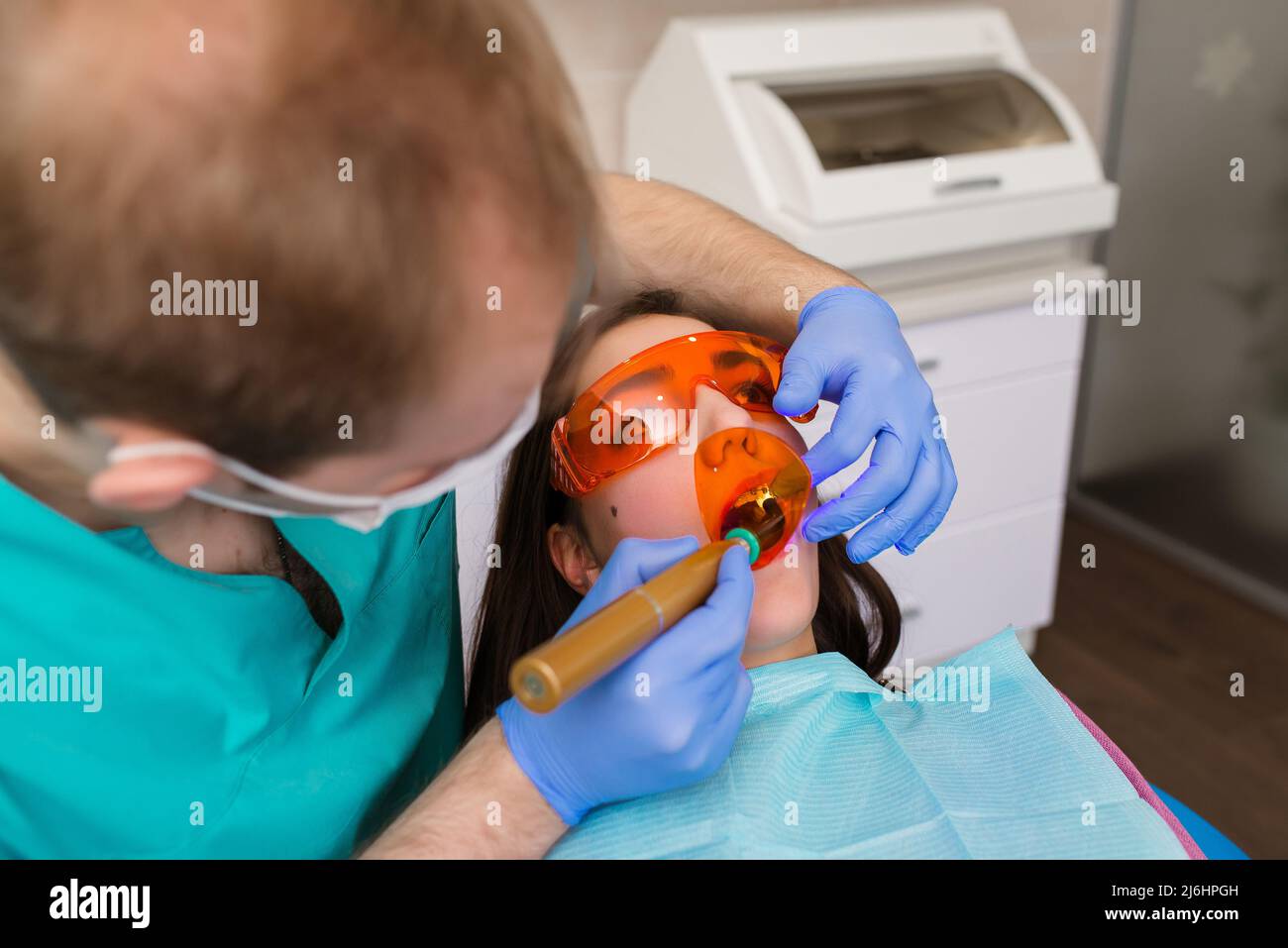 Eine Patientin in einer Zahnbrille behandelt die Zähne beim Zahnarzt mit ultraviolettem Licht. Zahnfüllungen Stockfoto