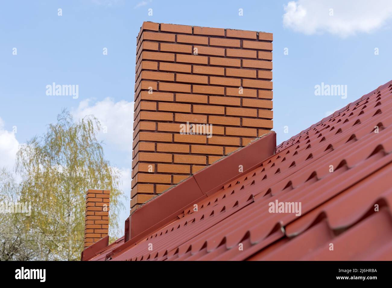Schornstein auf dem roten Metallkacheldach des Hauses gegen den blauen Himmel Stockfoto