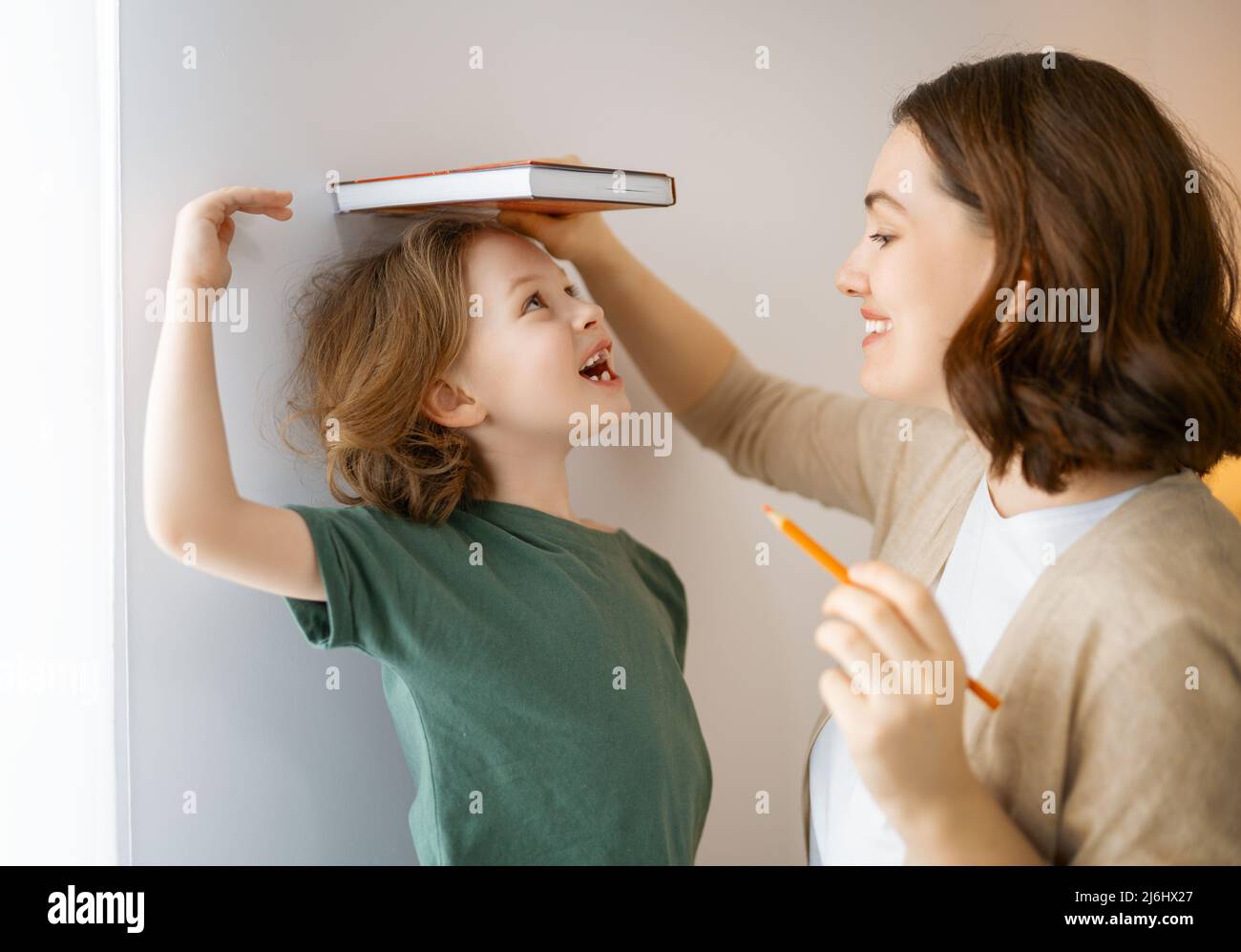 Kind und Mutter messen das Wachstum auf dem Hintergrund der Wand. Glückliche Familie zu Hause. Stockfoto