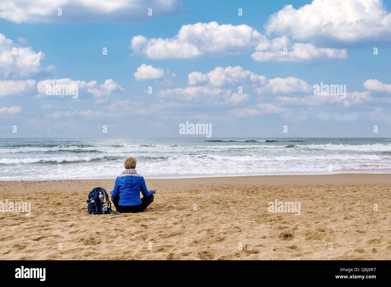 Frau, die am Strand sitzt und Meditation übt und den Horizont des Meeres beobachtet. Konzept von Spiritualität, Meditation und innerem Wachstum. Stockfoto