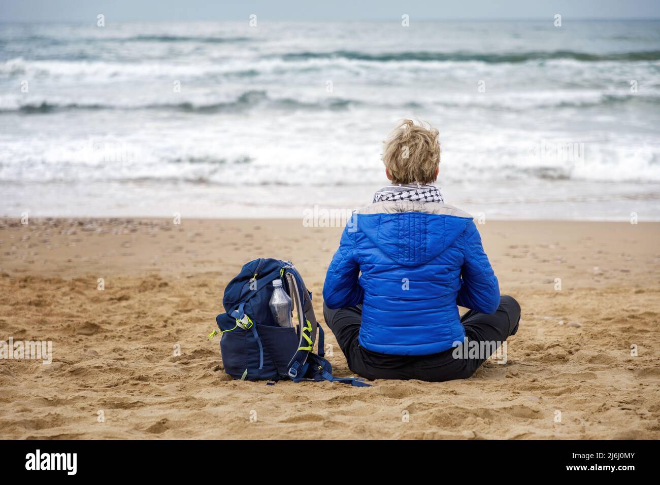 Frau, die am Strand sitzt und Meditation übt und den Horizont des stürmischen Meeres beobachtet. Konzept von Spiritualität, Meditation und innerem Wachstum. Stockfoto