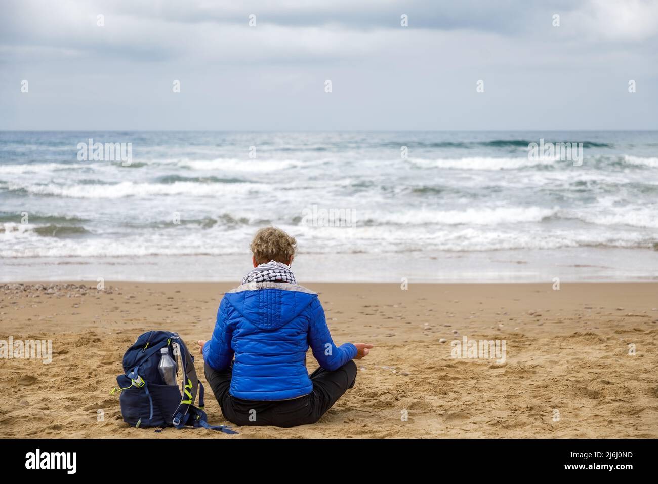 Frau, die am Strand sitzt und Meditation übt und den Horizont des stürmischen Meeres beobachtet. Konzept von Spiritualität, Meditation und innerem Wachstum. Stockfoto