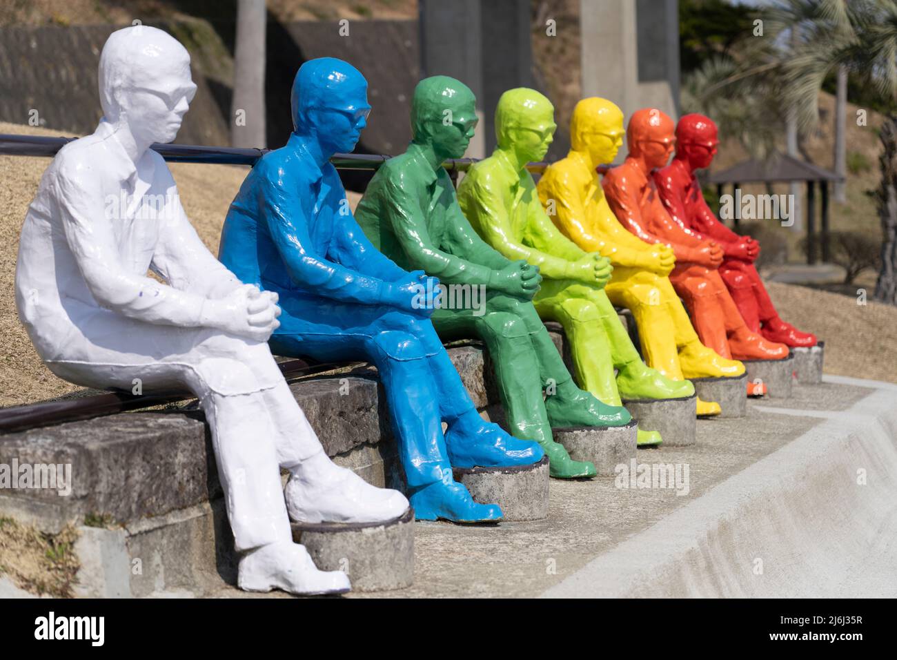 7 farbenfrohe Männerstatuen blicken auf den Ozean und die 7 Moai-Statuen in Sun Messe Nichinan, Miyazaki, Kyushu, Japan Stockfoto