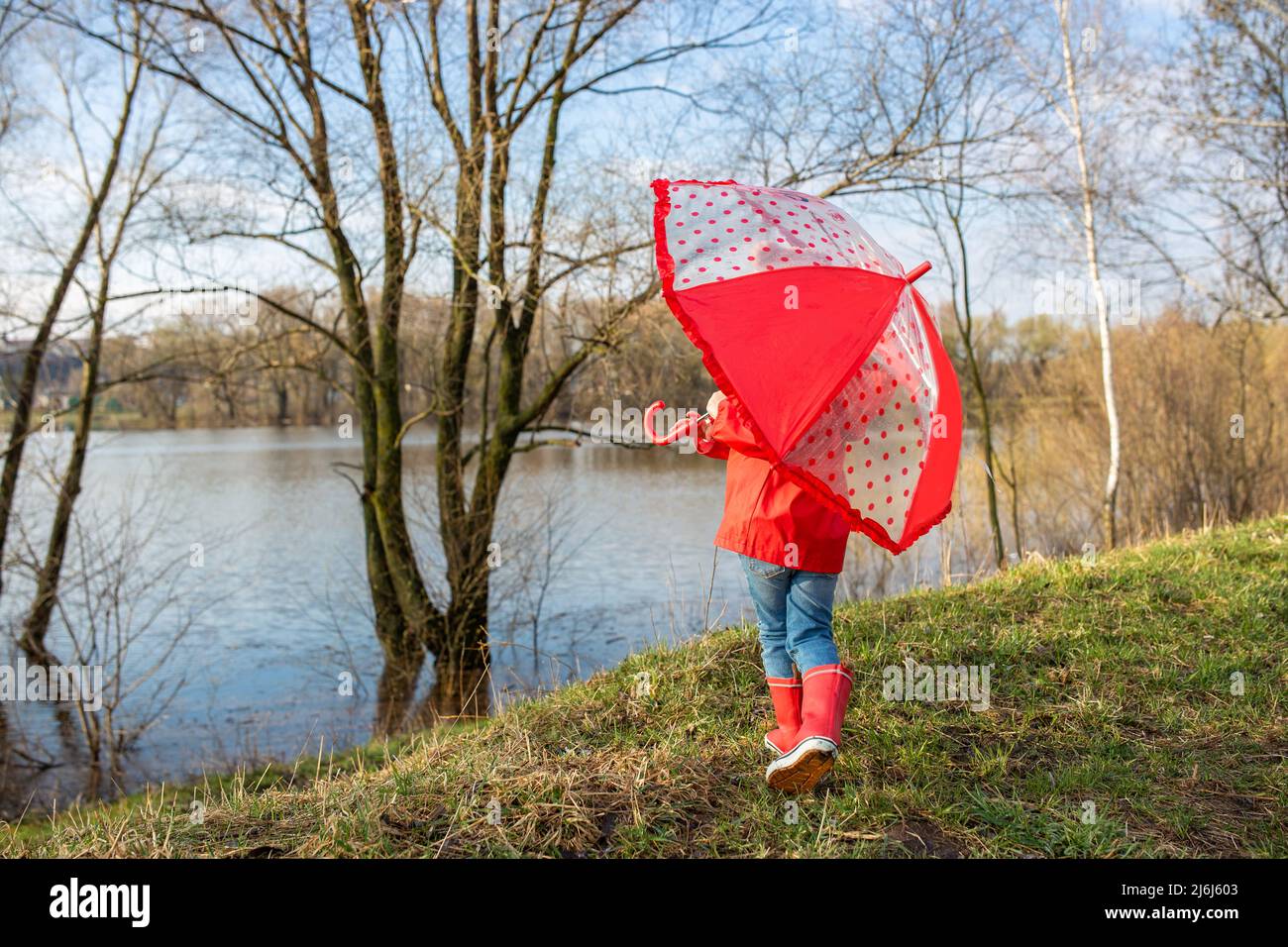 Kind spielt nach dem Regen mit Regenschirm in roten Gummistiefeln und Regenmantel. Stockfoto