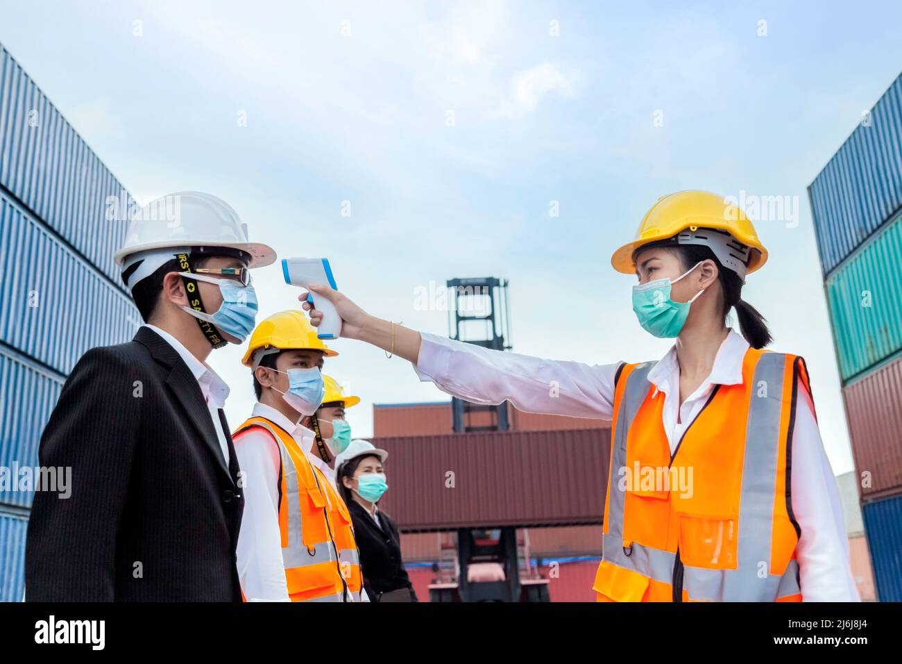 asiatischer Geschäftsmann trägt Gesichtsmaske Überprüfung Fieber durch digitales Thermometer vor dem Betreten der Arbeit in logistischen Frachtlager bei der Herstellung zu schützen Stockfoto