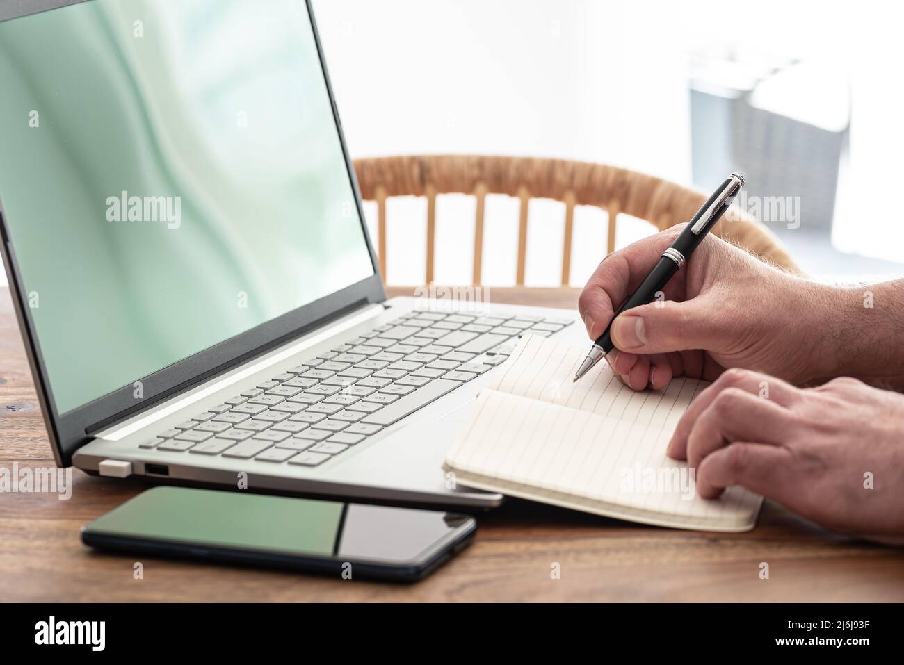 Ein Mann, der sich Notizen auf Papier macht, während er einen Laptop benutzt, E-Learning-Kurse macht oder von zu Hause aus arbeitet Stockfoto