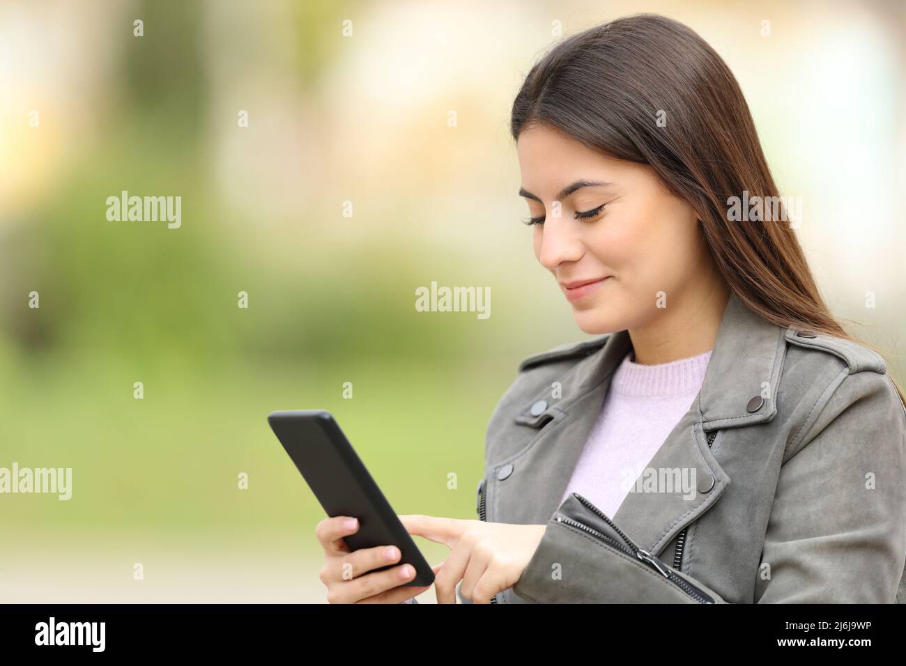 Zufriedener Teenager, der Smartphone benutzt, der in einem Park läuft Stockfoto
