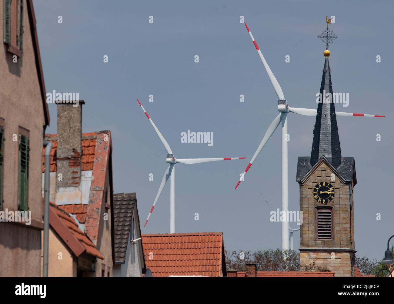 02. Mai 2022, Rheinland-Pfalz, Biedesheim: Windräder drehen sich hinter dem Kirchturm. Entlang der Autobahn A63 gibt es mehrere Windenergieanlagen. Foto: Boris Roessler/dpa Stockfoto