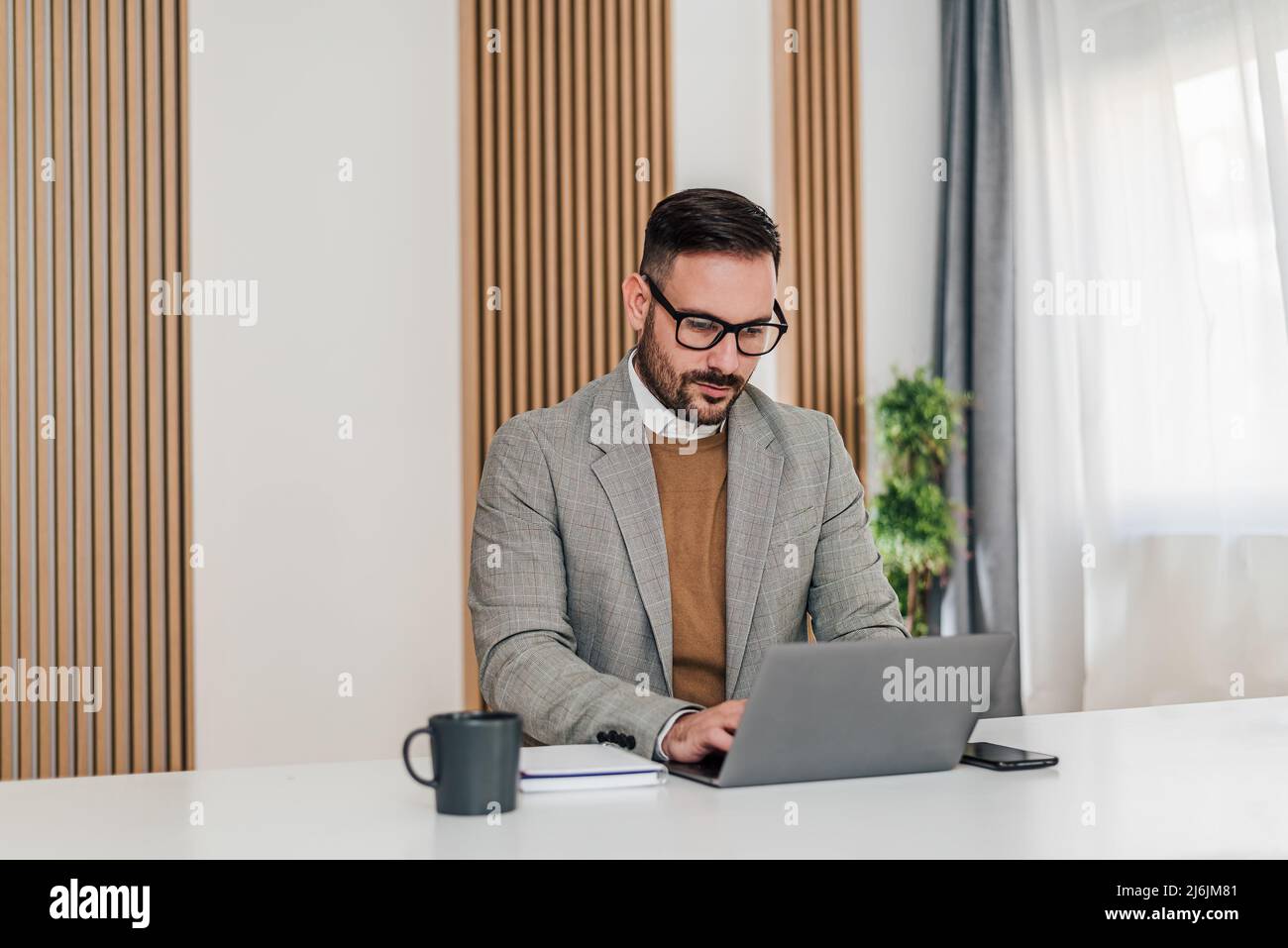 Selbstbewusster Geschäftsmann, der mit einem Laptop arbeitet. Fokussierter männlicher Unternehmer trägt Formalien. Er sitzt am Schreibtisch im Firmenbüro. Stockfoto