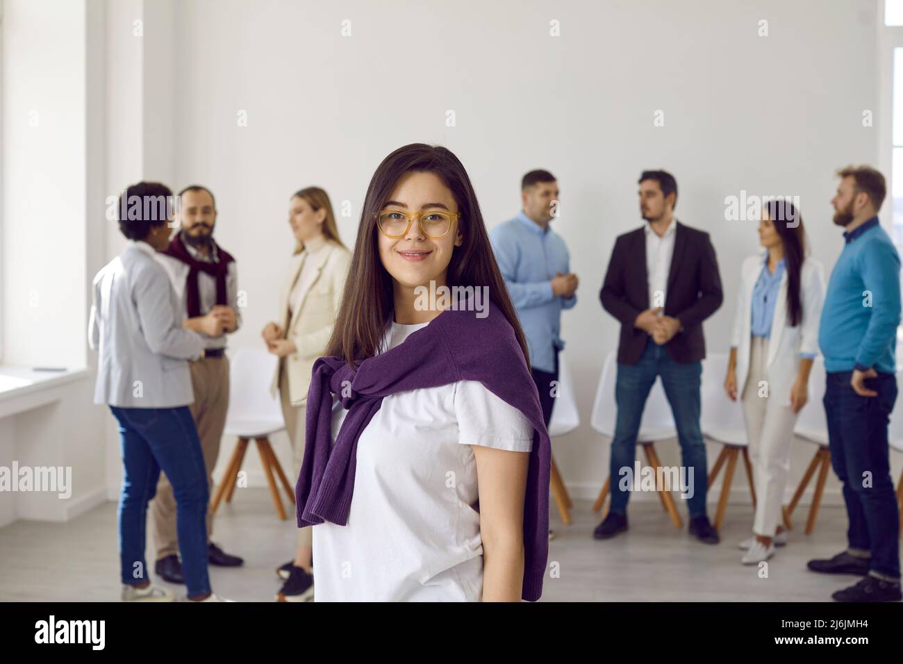 Attraktive Dame in Brillen posiert vor der Kamera im Büro, Geschäftsleute im Hintergrund Stockfoto