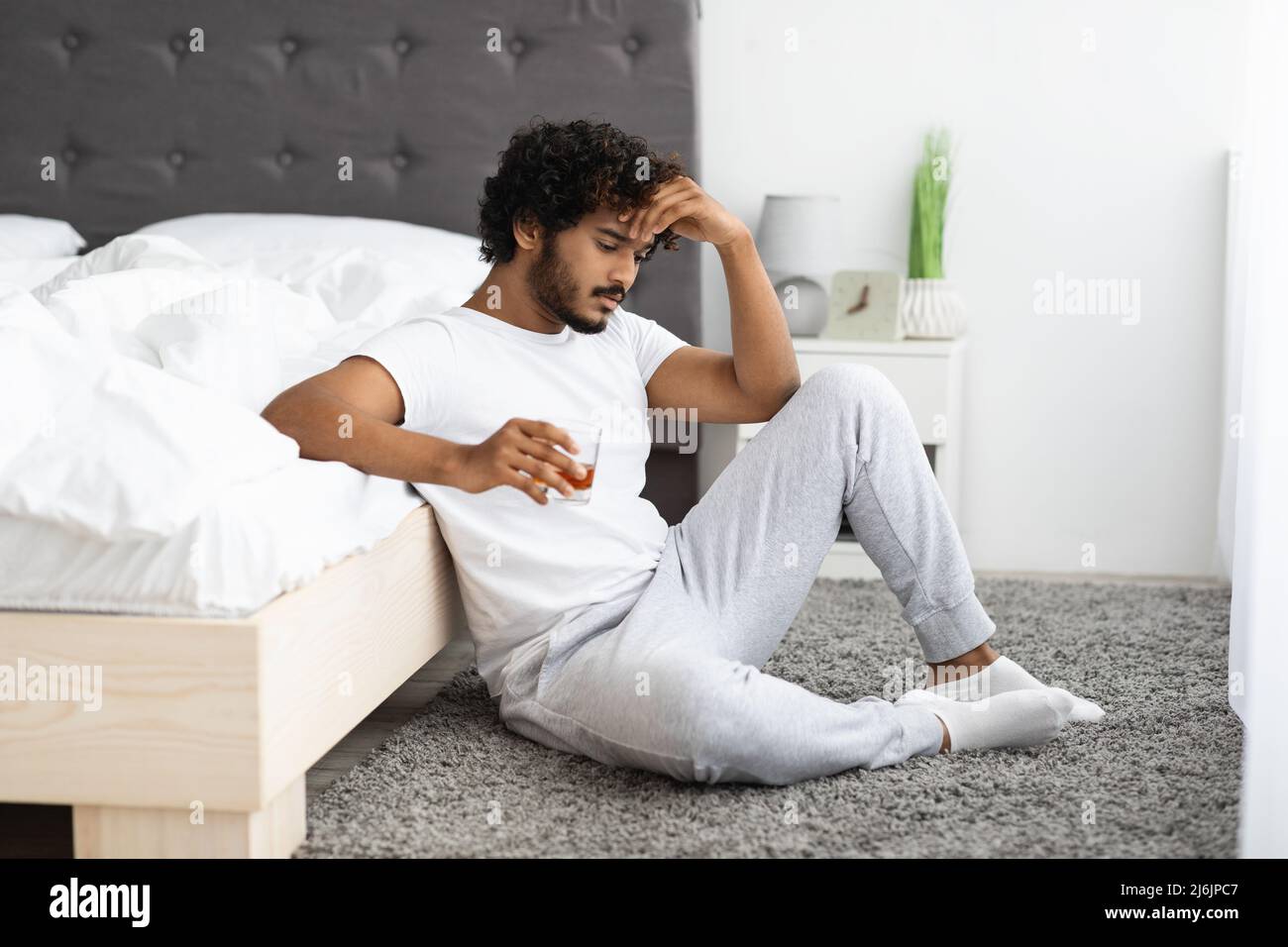 Depressiver hindu, der Alkohol trinkt und am Bett auf dem Boden sitzt Stockfoto