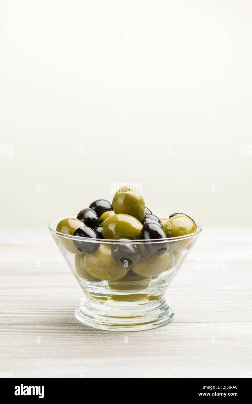 Große grüne und schwarze Oliven in Glasschüssel auf Holztisch Stockfoto