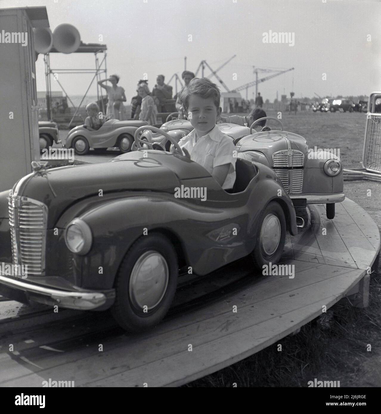 1950s, historisch, ein kleiner Junge, der in einer Autofahrt in Austin auf einem kleinen Vergnügungspark am Meer, England, Großbritannien, sitzt. Bei diesen Fahrten auf der Rennstrecke haben Kinder Spaß daran, Erwachsene zu spielen und ihr eigenes Austin J40 Auto zu fahren, das auf dem 1948 A40 basiert. Sie wurden als „Junior“ bezeichnet und mit Metallabschnitten aus der Longbridge-Fabrik in Austin hergestellt, wo sie als „Joy Cars“ bekannt waren, ein Name, der auf dem Nummernschild des Prototyps „Joy 1“ zurückgeht, der 1946 vorgestellt wurde. Die Produktion des Austin Junior 40 begann 1949 in einer Fabrik in Bargoed, Südwales, die sich speziell dort befand, um arbeitslosen ehemaligen Bergleuten Arbeit zu geben. Stockfoto