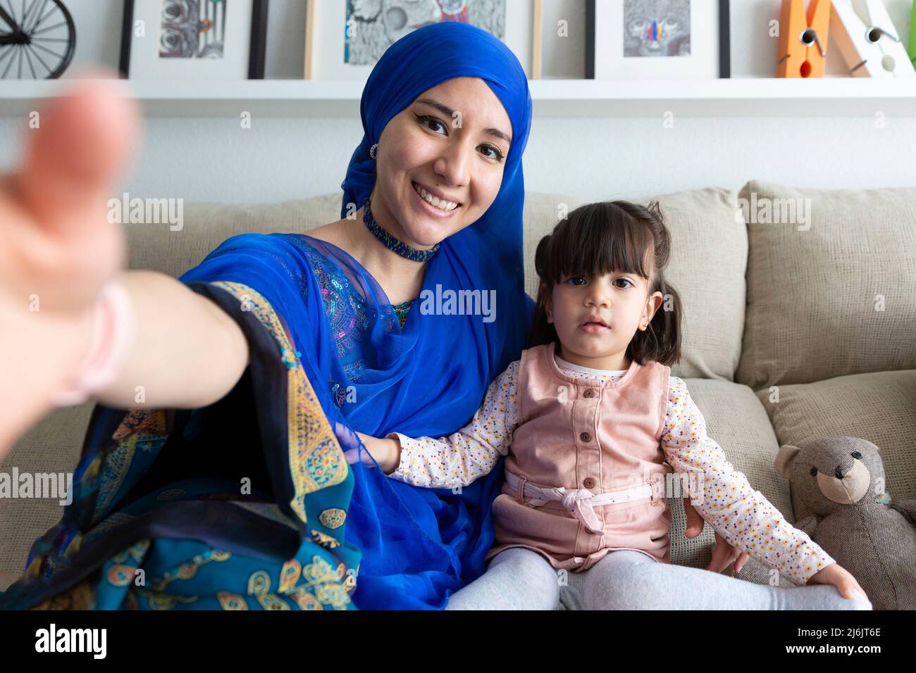 Junge muslimische Frau, die mit ihrer kleinen Tochter ein Selbstporträt anfertigen kann. Alleinerziehende Familie, die eine lustige Zeit zu Hause hat. Stockfoto