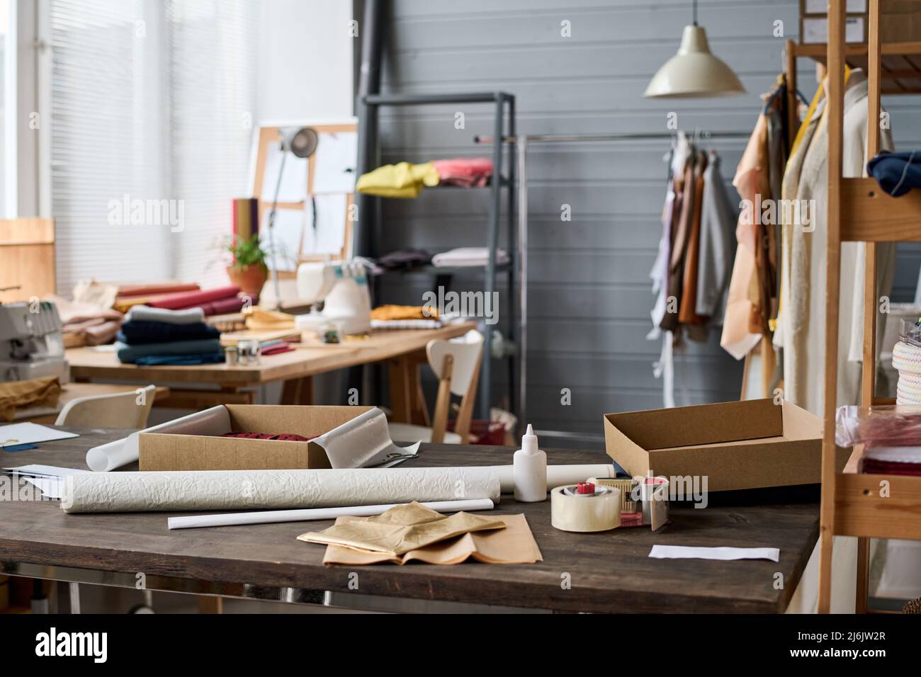 Interieur der geräumigen modernen Werkstatt des Schneiders oder kreativen Modedesigners mit unfertigen Kleidern, die auf Regalen und anderen Sachen hängen Stockfoto
