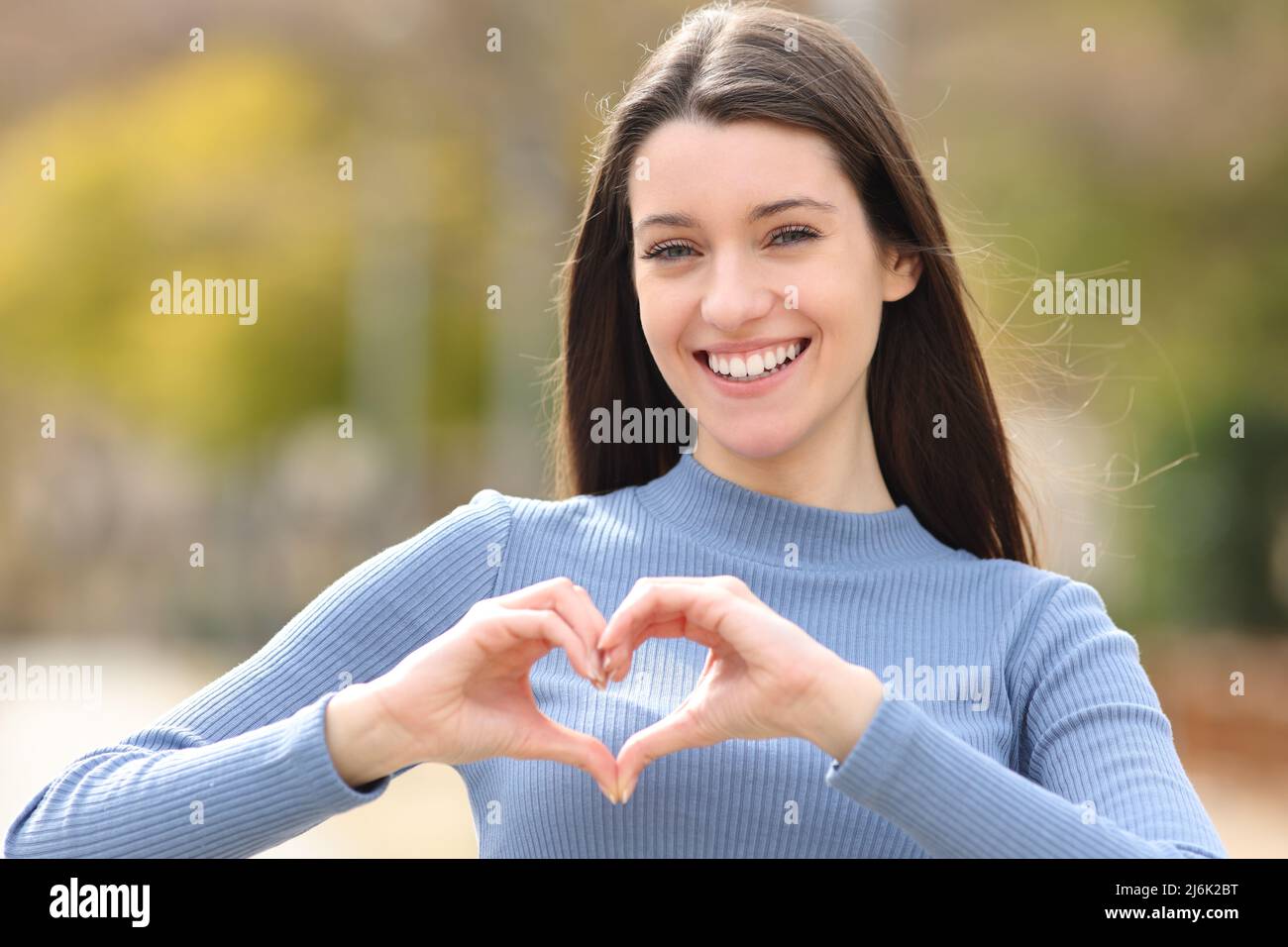 Vorderansicht Porträt einer glücklichen Teenagerin, die mit ihren Händen in einem Park herzförmig macht Stockfoto