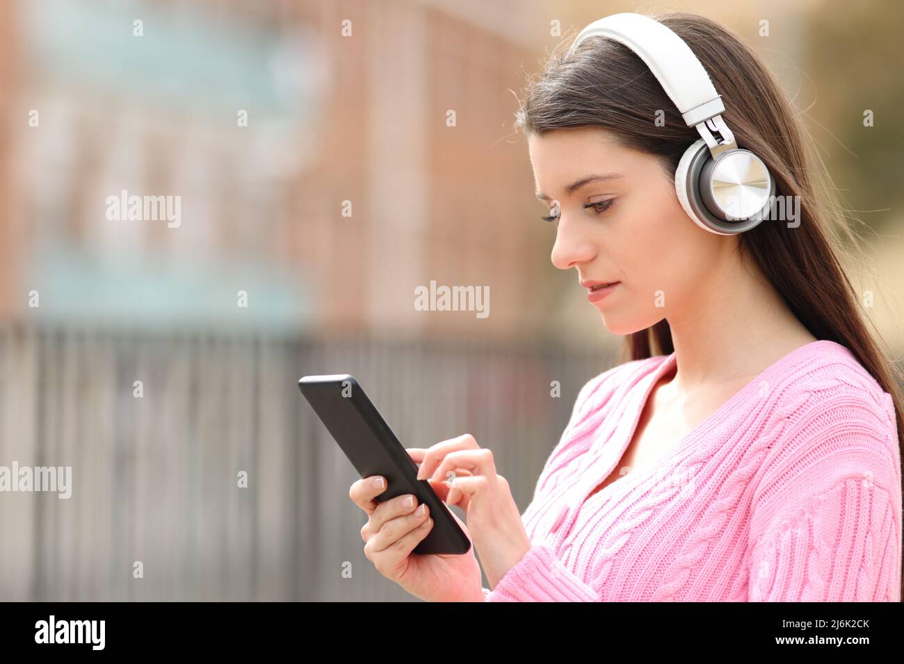 Seriöse Teenager hören Musik mit Kopfhörern, die auf der Straße am Telefon surfen Stockfoto