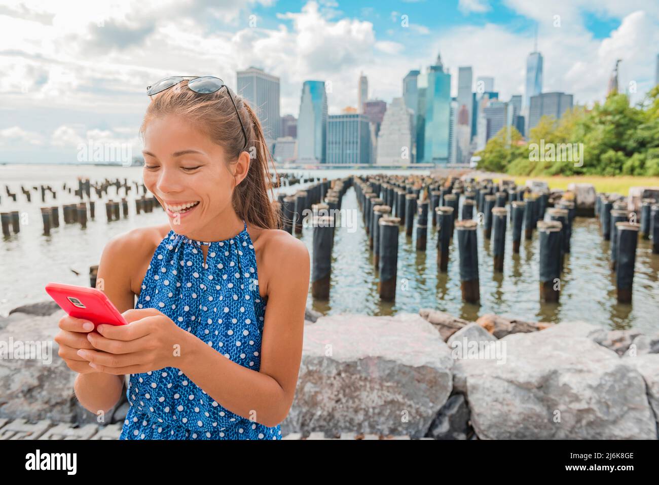 New York Tourist Frau mit App am Telefon von Manhattan City Skyline Waterfront. Menschen, die vom Brooklyn Bridge Park aus die Aussicht auf die Innenstadt genießen Stockfoto