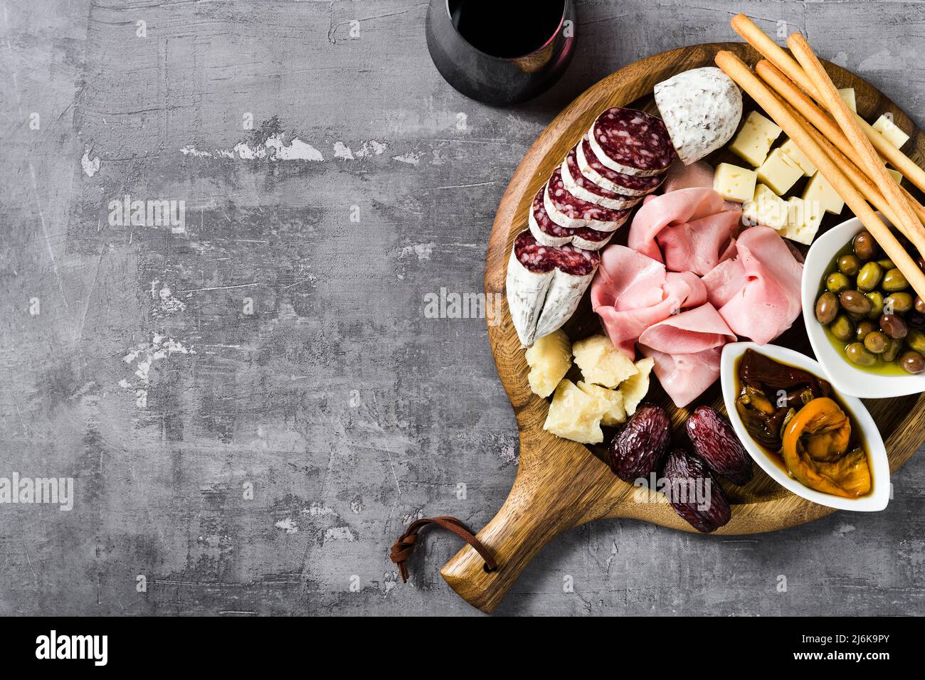 Italienische Snacks und Antipasti auf einem Tablett und Rotwein: Prosciutto, Salami, getrocknete Tomaten, Oliven, Käse, grissini und Termine. Sommerjause Stockfoto