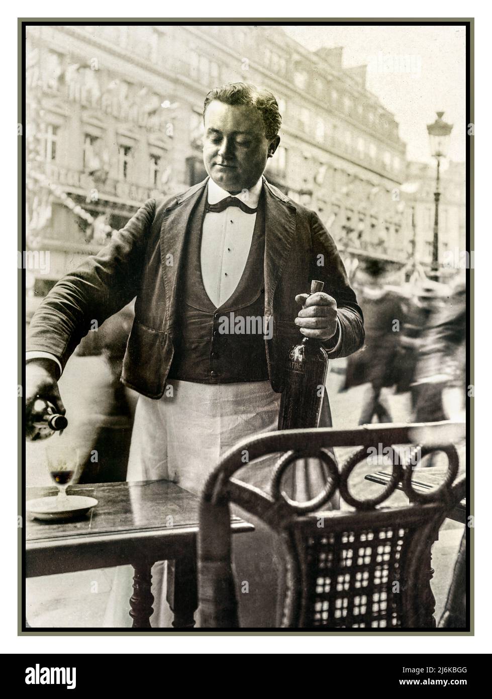 Paris Waiter 1900s Vintage Retro B&W serviert Wein im Straßencafé-Restaurant Boulevard in typisch französischer Kellneruniform und gießt ein Glas Rotwein vor der Außenfassade von Paris France Stockfoto