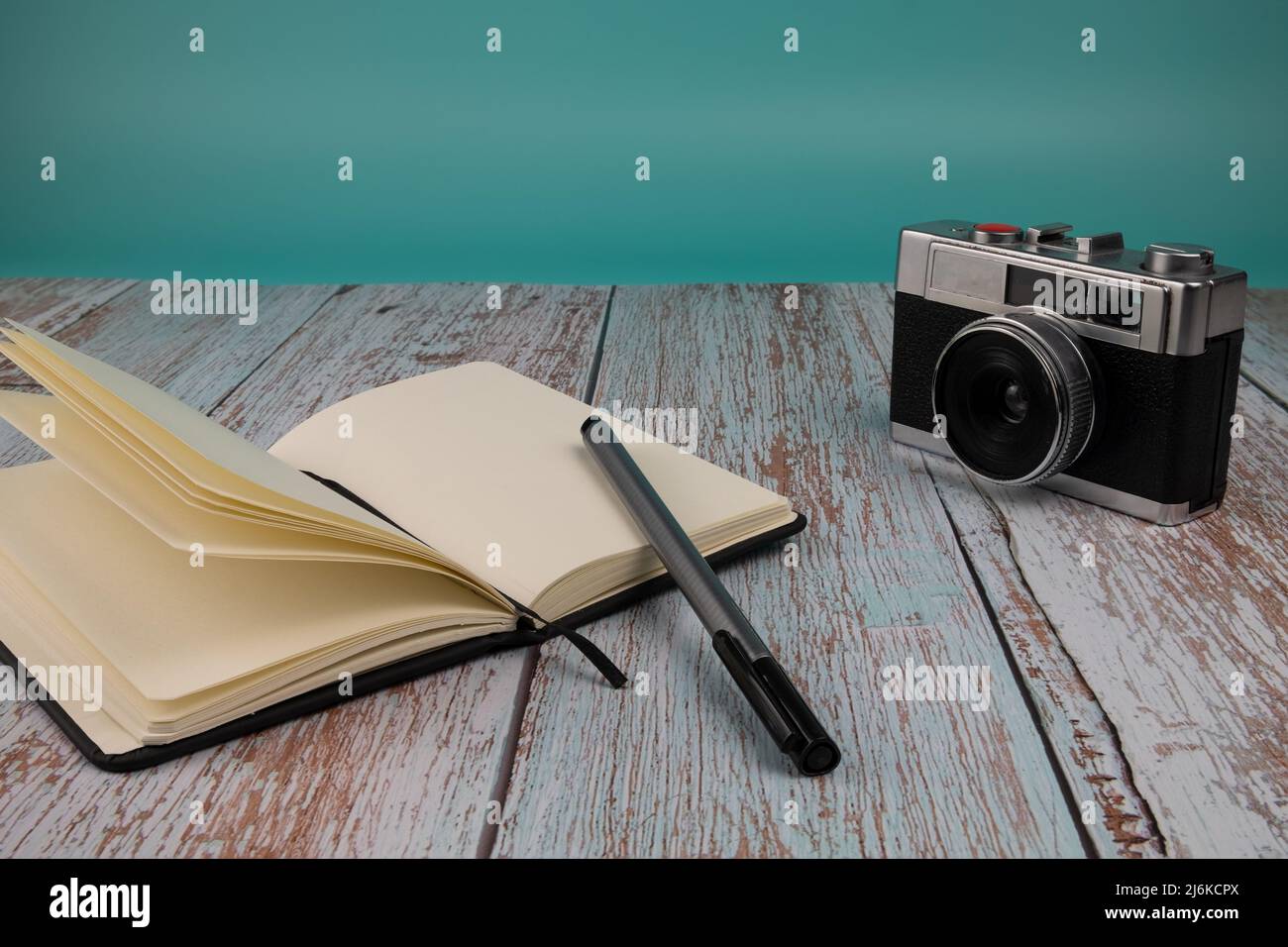 Notizbuch mit einem Stift und einer Fotokamera, auf einem Holztisch mit hellblauem Hintergrund. Konzept der freien Zeit. Stockfoto
