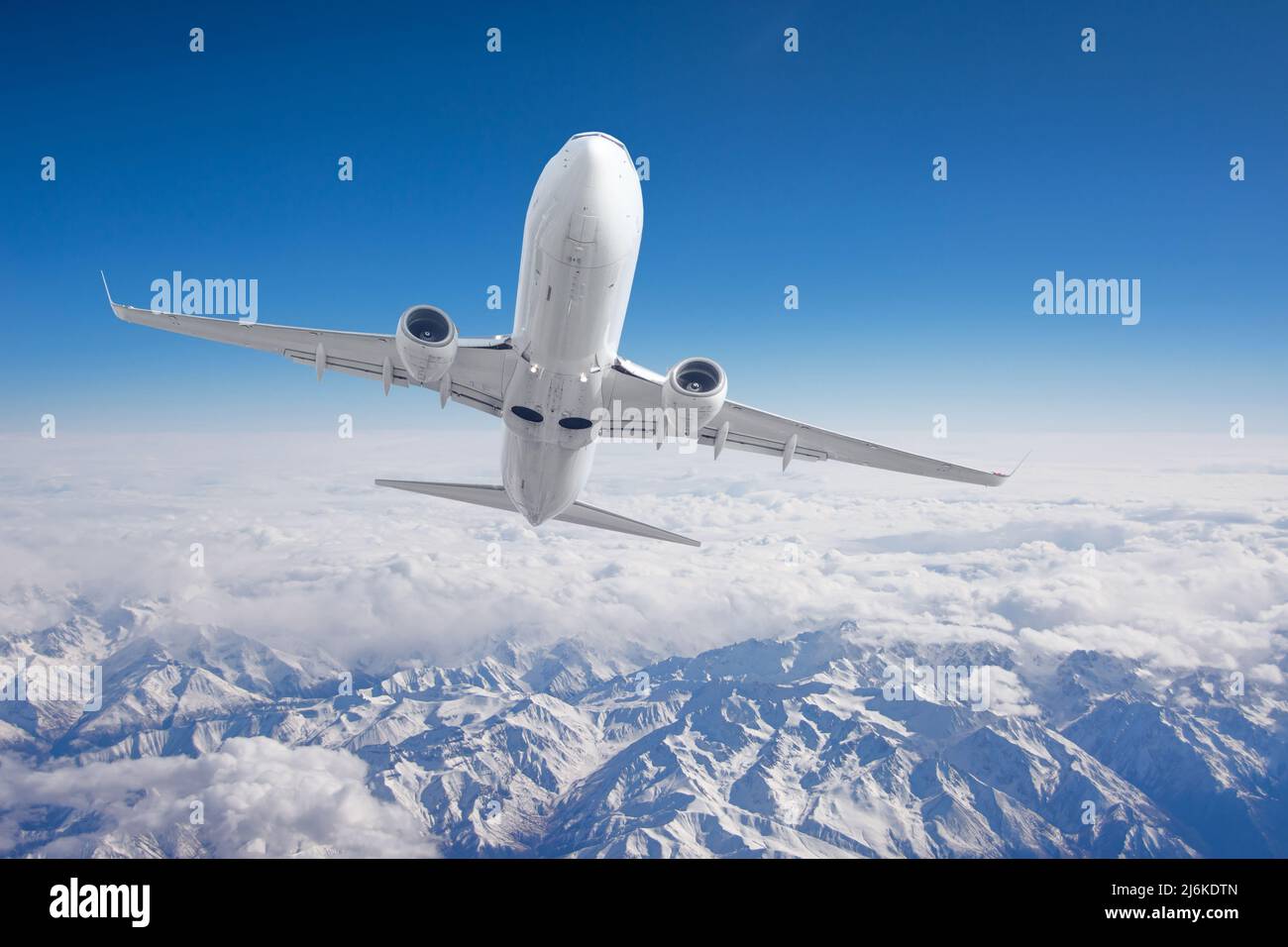 Luftaufnahme Berge aus dem Flugzeug. Fliegen Sie über das schneebedeckte Bergtal bei reinem Sonnenschein mit vorbeiziehenden Wolken Stockfoto