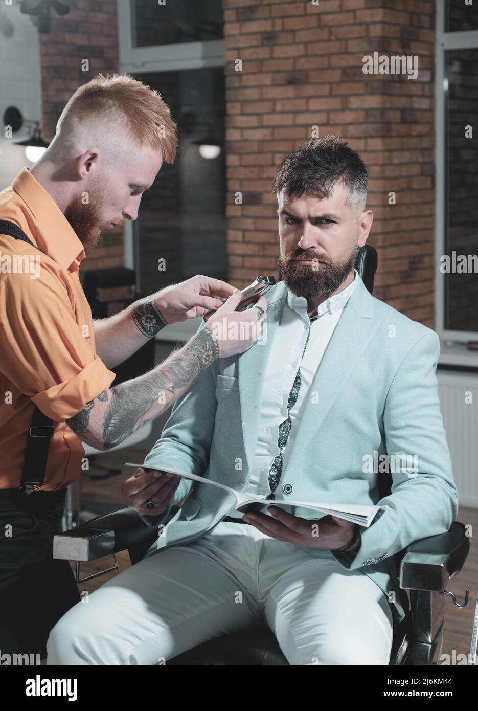 Barbier, der im Friseurladen einen attraktiven bärtigen Mann Frisur macht. So trendig und