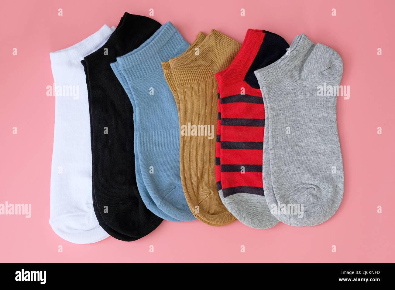 Bunte kurze Socken für sportliche Aktivitäten. Baumwollsocken in grau, braun, schwarz, blau von oben. Mehrere Paar verschiedene Socken auf einem rosa Rücken Stockfoto