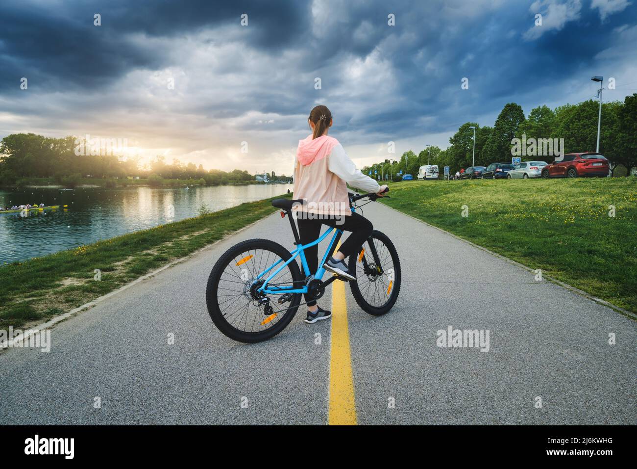 Frau, die bei Sonnenuntergang auf der Straße in der Nähe des Sees mit dem Mountainbike unterwegs ist Stockfoto