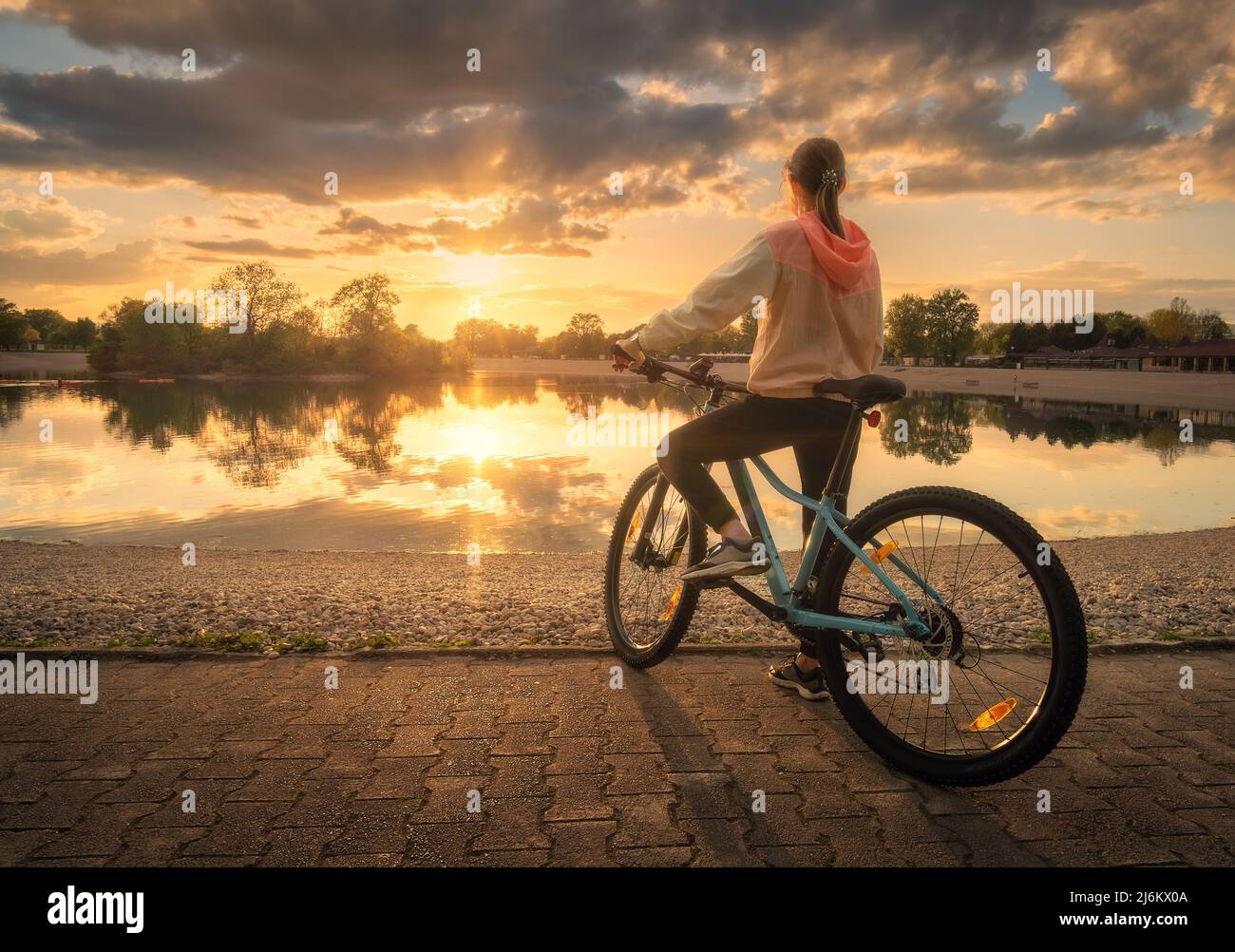 Frau auf dem Mountainbike in der Nähe des Sees bei Sonnenuntergang im Sommer Stockfoto