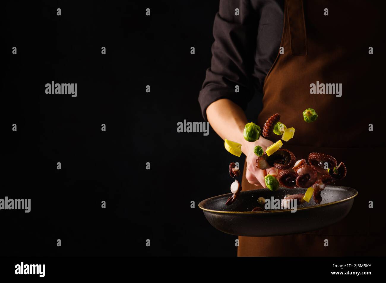 Der Prozess des Kochens von Meeresfrüchten mit Gemüse in einer Pfanne von einem professionellen Koch auf schwarzem Hintergrund. Levitation. Bio-Lebensmittel, Rezeptbuch, gehen Stockfoto