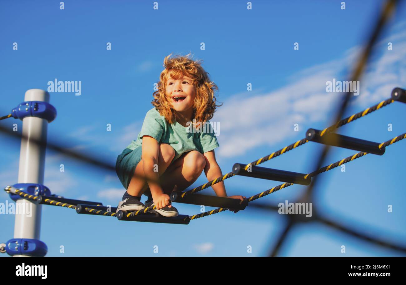 Netter Junge klettert die Leiter auf dem Spielplatz hoch. Kind klettert die Leiter gegen den blauen Himmel hinauf. Platz für Text kopieren. Stockfoto