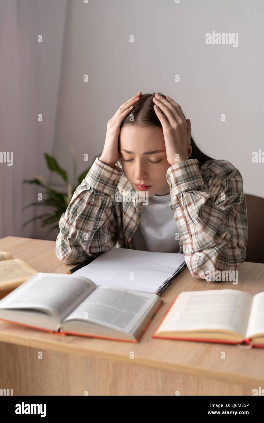 Müder Student Teenager, der Kopfschmerzen oder müde fühlt, während er Hausaufgaben zu Hause macht. Depressive kranke Schüler, die allein studieren, sorgen sich, Bildungsprobleme Stockfoto