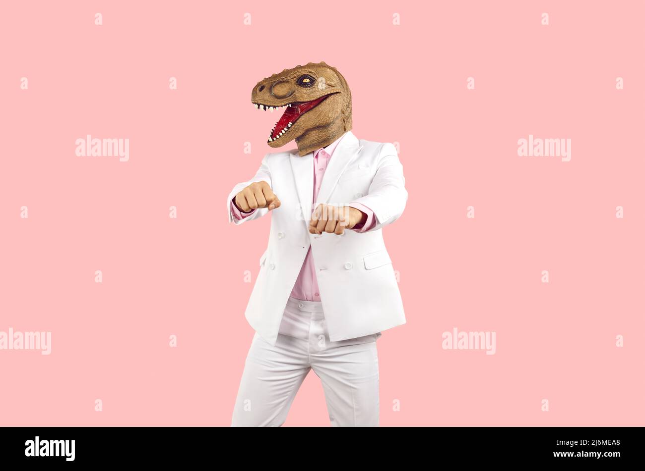 Seltsamer Typ im Anzug und lustige Dinosaurier-Maske tanzen vor rosa Studio-Hintergrund Stockfoto