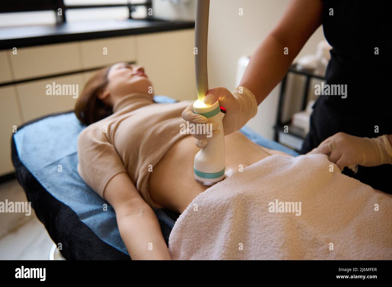 Schöne junge Frau auf einem Tagesbett erhalten Hardware-Spa-Verfahren für Cellulite-Reduktion und Gewichtsverlust in der medizinischen Klinik. Stockfoto