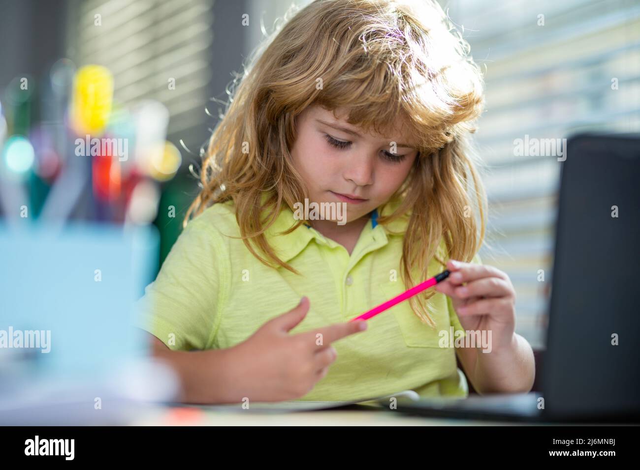 Portrait Schulkind sitzt auf dem Tisch und macht Hausaufgaben. Kind mit Bleistift und Schrift. Junge, der auf weißem Papier am Tisch zeichnet. Grundschule und Stockfoto