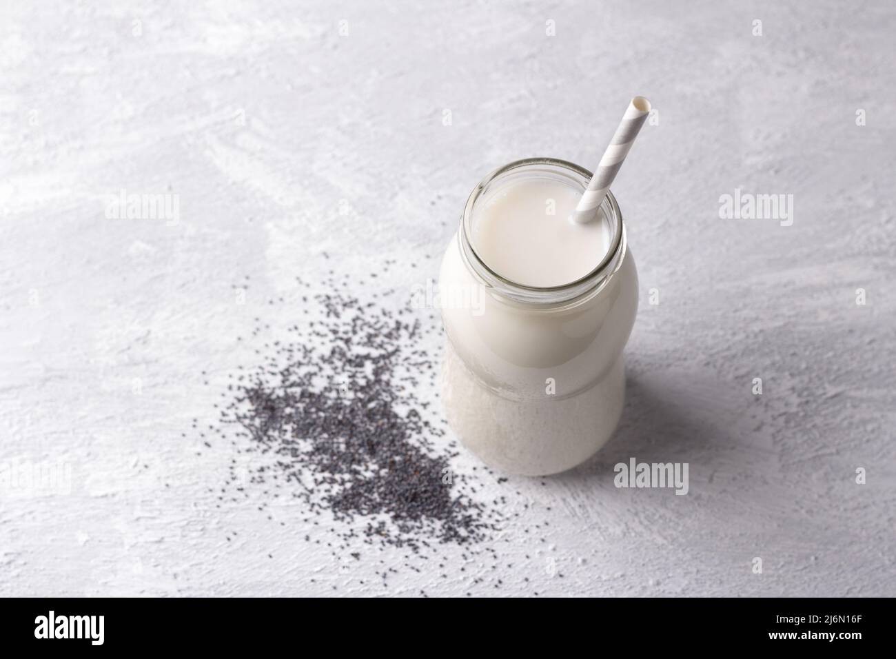 Frische Mohnmilch in der Flasche mit Samen auf hellem Hintergrund. Gesunde Ernährung, veganes Getränk, alternative Milch. Freiraum Stockfoto