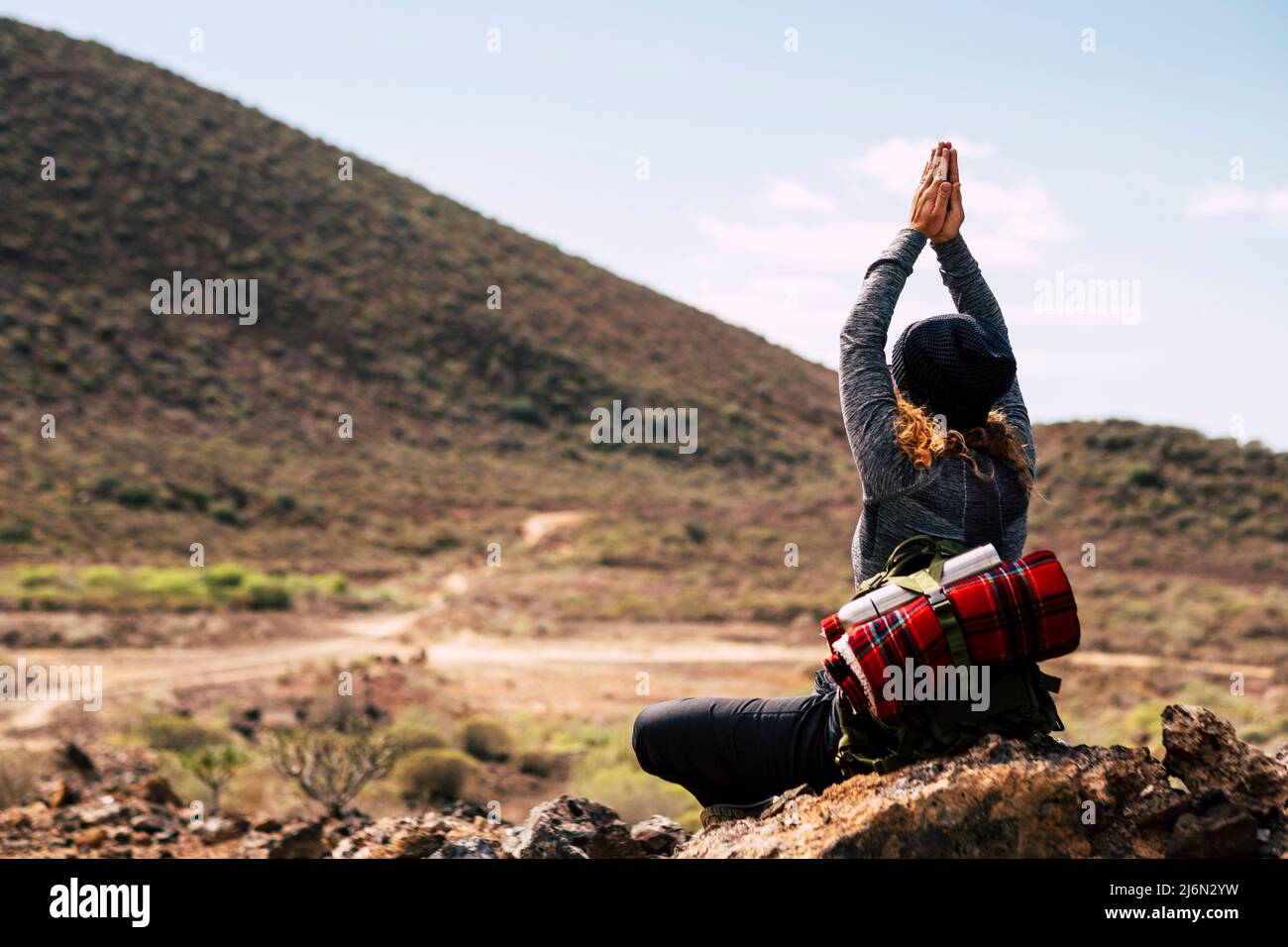 Rückansicht einer Frau, die meditiert, indem sie die Hände auf einem Felsen zusammenschließt. Frau, die die Natur während des Trekkings erkundet. Frau meditiert im Gebet Pose auf felsigen Stockfoto