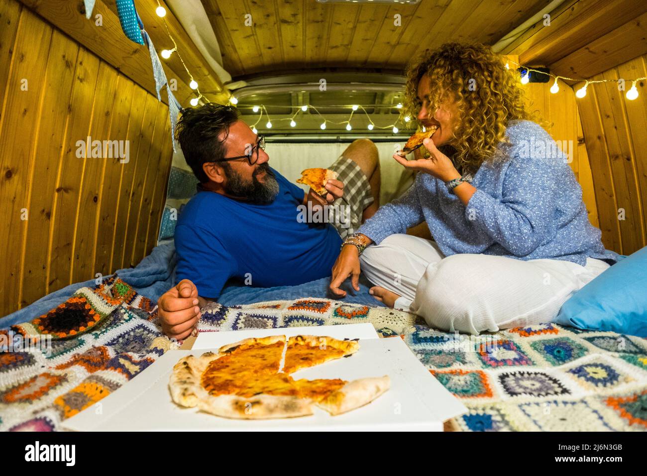 Pärchen haben Spaß beim Essen von Pizza in einem handgefertigten Oldtimer-Kleinbus in einem alternativen Lebensstil und Reiseurlaub - glückliche, romantische Menschen genießen es Stockfoto