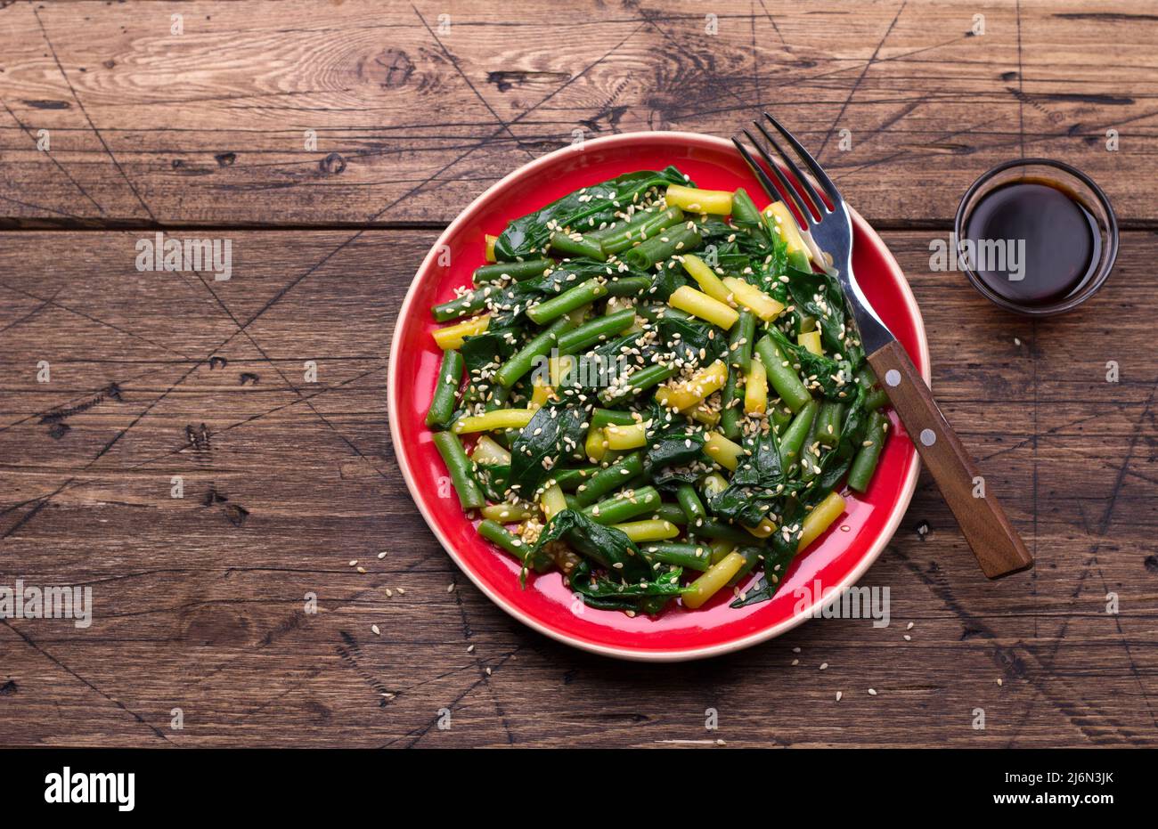 Grüne und gelbe Bohnen mit Spinat, Sesam und Sojasauce auf Holztisch, Draufsicht, Freiraum Stockfoto